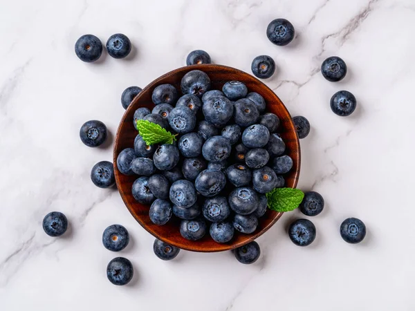 Sweet blueberries on a wooden plate over marble surface. Ripe juicy wild berry for vegetarian dessert. Blueberry as natural antioxidant for detox diet. Vitamin vegan snack. Top view.