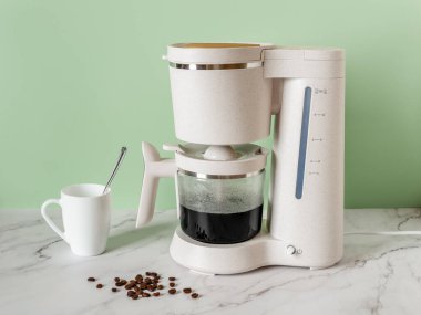 Otomatik damlayan kahve makinesi sabah içkisini demler. Elektrikli kahve makinesi evdeki mermer tezgahın üstünde cam demliği sıcak sade kahveyle dolduruyor. Ev aletleri. Kahvaltı konsepti. Ön görünüm.