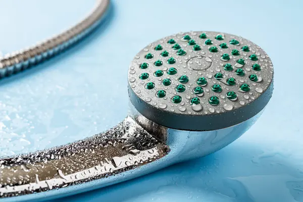 Islak el yapımı duş başlığı makrosu. Metal bir duş başlığına su damlıyor ve mavi arka planda esnek bir hortum var. Duş al, yıka, hijyen ve banyo konsepti. Yakın plan..