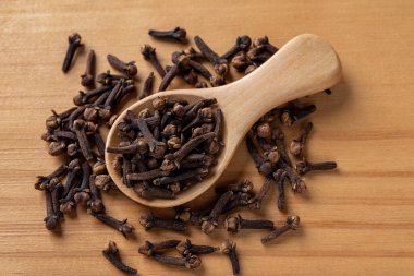 Ahşap arka planda kaşık içindeki tüm baharat karanfili. Tahta kaşık dolusu kuru karanfil tomurcukları makro. Baharat ve bitkisel tıp konsepti. Üst görünüm.