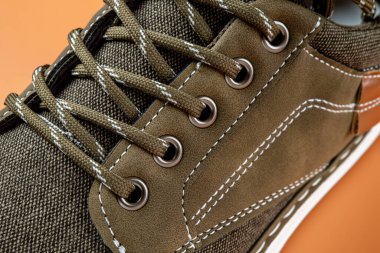 Turuncu arka planda haki rengi spor ayakkabıların dantelleri ve göz dirsekleri. Aktif yaşam tarzı, yürüyüş ve koşma için beyaz tabanlı yeni kahverengi tekstil ayakkabıları. Yakın plan..