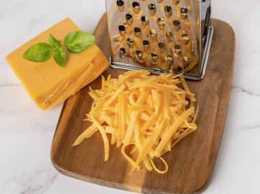 Whole and shredded cheddar cheese close-up. Heap of grated orange cheese and metal grater on a wooden cutting board. Milk protein, calcium concept. Top view.