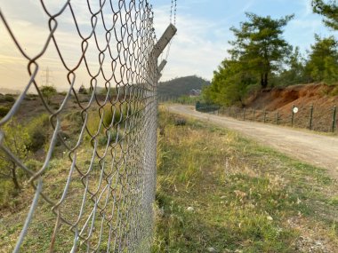 Demir çit ve dikenli tel toprak yola paralel. Kırsalda gün batımı. seçici odak çit duvarı.