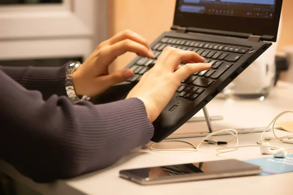 young girl works at computer, typing something on laptop keyboard.