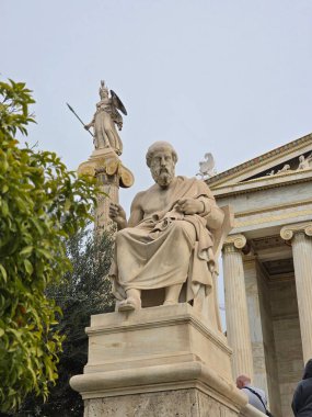 Ünlü bir antik filozofun mermer heykeli Atina 'da belirgin bir şekilde duruyor. Arka planda görünen bir sütunun tepesinde Tanrıça Athena, tarihi önemi ve sanatsal ayrıntıları gözler önüne seriyor..