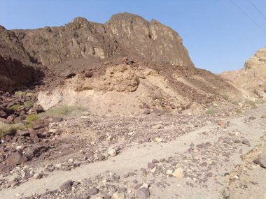 Kaya oluşumları kurak araziye hükmediyor, toprak ve taşın katmanlarını sergiliyor. Sahne, güneşli bir günde bir çöl ortamının engebeli güzelliğini yakalar..