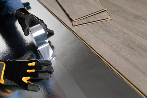 安装浮动地板 工作人员放置衬垫层压板用胶带 住房改善概念 图库图片