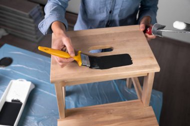 Young women preparing to restore a stepladder for children as a hobby house improvement. Pouring paint into a bucket on a table.	