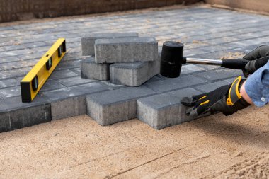İnşaat işçisi kaldırıma eldiven ve lastik çekiçle beton döşemiş. Ev geliştirme.