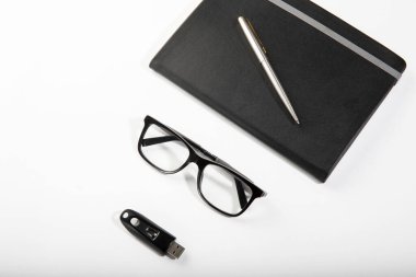 Bir defter, kalem, siyah gözlük ve USB çubuğu ile düzenli bir çalışma alanı düzeneği..