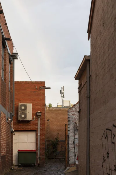 Urban back alleyway features an industrial waste bin and a mobile phone tower, highlighting the blend of modern infrastructure.