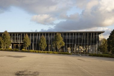 Boş bir otoparkla çevrili modern ofis binası huzurlu bir şehir manzarası sunar..