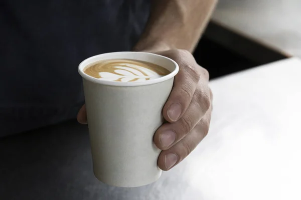 Hand holding a takeaway coffee cup filled with aromatic coffee, featuring heart-shaped latte art foam.