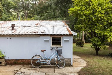 Eski metal yapının yanında duran mavi basamaklı çerçeve bisiklet.