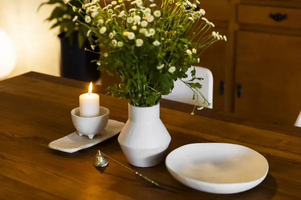 Wooden dining table with a flower vase, a burning candle, and a candle snuffer, creating a warm and inviting ambianc