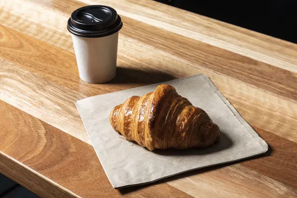 Ayçöreği ve paket kahveyi kağıt bardakta, ahşap bir arka planda..