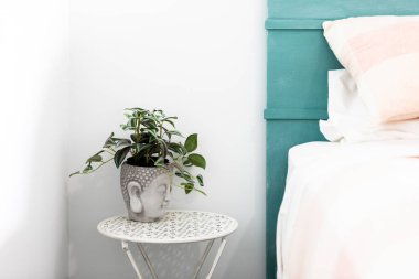 Buda 'nın baş bitkisinin içine komodinin üzerine yerleştirilmiş ev bitkisi yatak odasının iç dekorasyonuna huzur verici bir dokunuş katıyor..