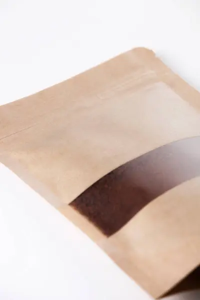 Brown kraft paper bag filled with ground coffee on a white background.
