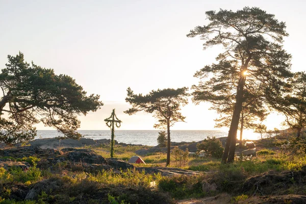 Roslagenの海岸線にキャンパーがいる小さなテント付きの古典的な真夏の極の日の出 スウェーデン ストック写真