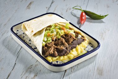 Dev bir Tex Meksiko dürüm tabağı, içi guacamole, yeniden kızartılmış fasulye, doğranmış et ve salata ile dolu, düz bir ekmeğin üzerinde. Mavi ahşap bir masada.