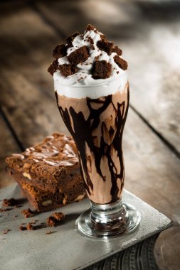 Krem şantili çikolatalı milkshake ve üzerinde browni parçaları olan ahşap bir masa.