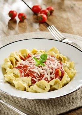 Tahta bir masada domates soslu, fesleğenli ve parmesanlı taze tortellini..