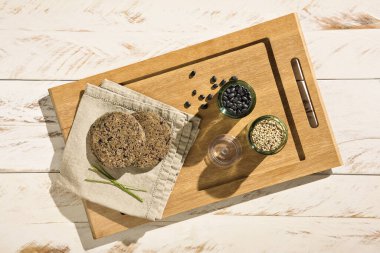 Ev yapımı sağlıklı vejetaryen kinoa ve ahşap tepside siyah fasulye burgeri, yukarıdan gelen malzemelerle birlikte.