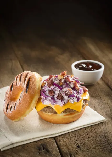 Donut burger with bacon, coleslaw, onion and cheddar cheese, on a wooden table