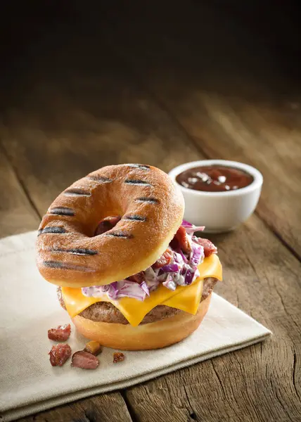 Donut burger with bacon, coleslaw, onion and cheddar cheese, on a wooden table