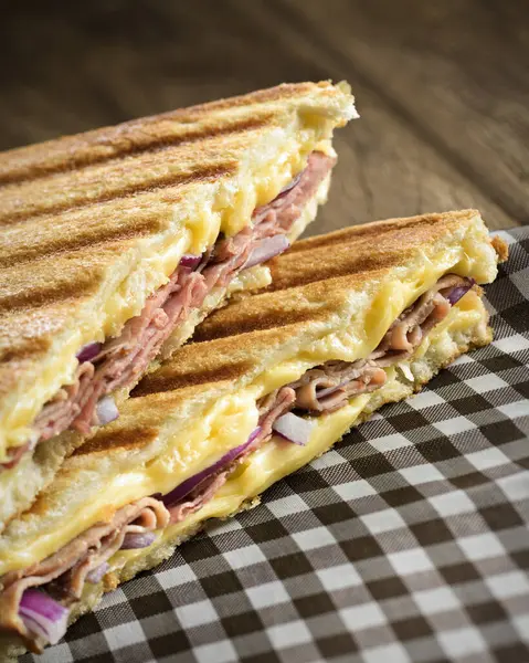 Ham and cheese sandwich on a checkered napkin, with melted cheese, ham and onion, on a toasted sliced bread.