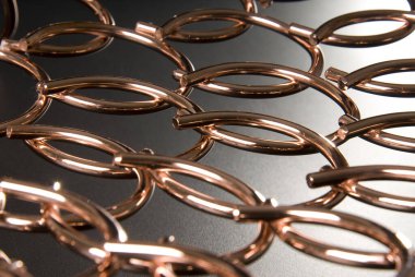 Siyah ve beyaz arka planda, birbirlerine konulmuş soyut bronz halkalar