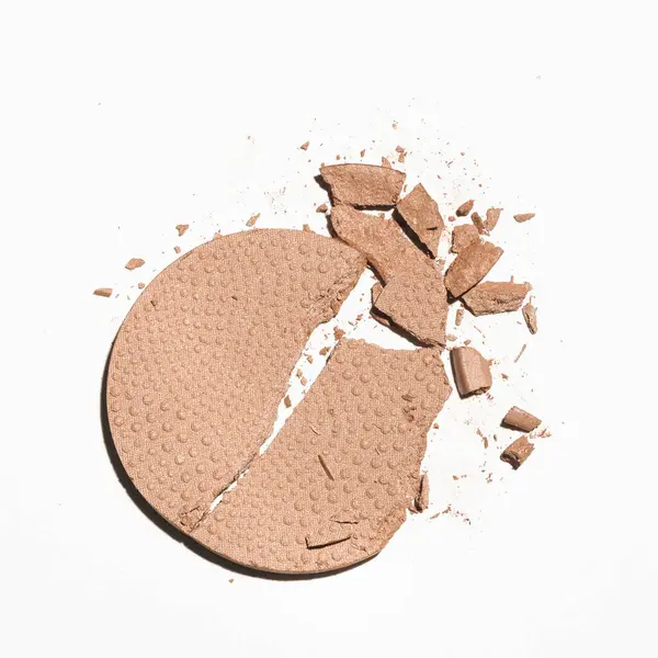 A makeup product, cracked in pieces on a white background