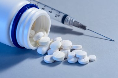 Arkasında şırınga olan plastik bir konteynırdan dökülen beyaz hapları mavi ışığa yakın.