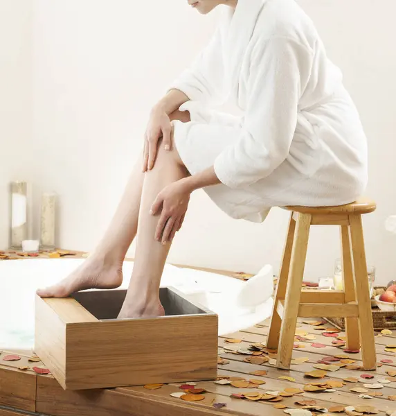 Ayaklarını ıslatan bir kadın, rahatlatıcı bir ayak banyosu, küvetin yanındaki ahşap bir kasede..