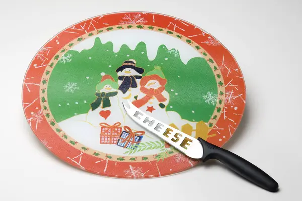 Christmas themed round glass cutting board with three snowman illustration and a cheese knife, isolated on white