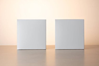 İki beyaz kare kutu, yan yana, aydınlık bir arka planda izole edilmiş.