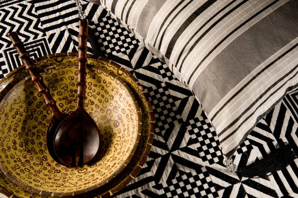 Siyah beyaz bir yatak örtüsünün üzerinde kaşıkla salata kasesi ve yanında yastık.