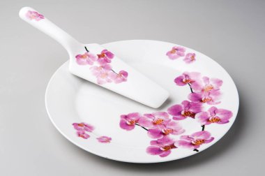 Yuvarlak pasta tabağı ve kek küreğiyle, orkideler basılı, izole