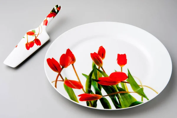 Yuvarlak pasta tabağı ve kek küreğiyle kırmızı lale izole edilmiş.