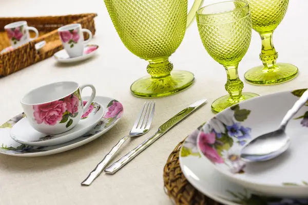 Table set up with dinnerware, silverware, jar and cups of glass on table cloth