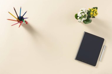 Tablet, kalem, çiçek ve renkli kalemle temiz bir arkaplanda, masanın üst görünümü