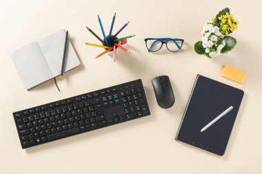 Tabletli ve kalemli masanın üst görünümü, çiçekler, klavye ve fare, kitapçık, otomatik kalem, yapışkan not, gözlük ve renkli kalem, temiz bir arkaplan üzerinde