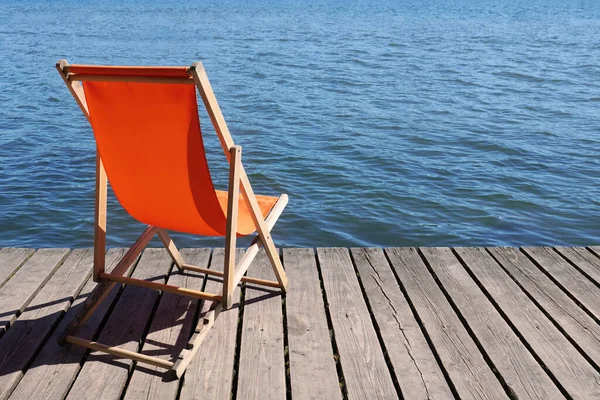 木制甲板上的空的可折叠的海滩椅子 上面可以看到平静的湖水 还有可复制的空间 免版税图库照片