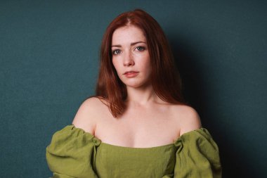 Kızıl saçlı aktris yeşil bir elbiseyle stüdyonun vesikalık resmi için yeşil arka planda poz veriyor.