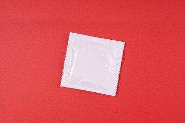 Kırmızı zemin üzerinde beyaz kare alüminyum folyo paketi ve kopyalanmış prezervatif