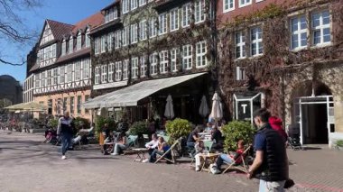 Hannover, Aşağı Saksonya, Almanya - 15 Nisan 2025: İnsanlar Ballhofplatz eski kasaba meydanındaki açık hava sokak kafesinde güneşli bir bahar gününün tadını çıkarıyorlar.