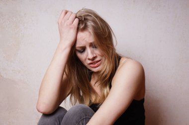 Makyajını boyamış, ağlayarak başını tutup üzüntüsünü ve umutsuzluğunu ifade eden genç bir kadın.