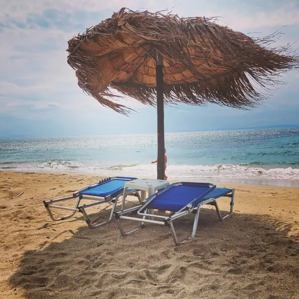 Rüzgarlı bir günde kumlu sahilde güneşli yataklar ve şemsiye. Rahatlama, tatil, dinlenme, tatil kavramı. 