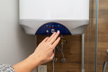 Kadın eli su ısıtıcısının enerjisini açıyor.