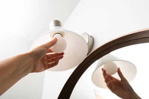 Woman hand changing lamp in modern bathroom